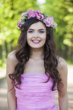 Sağlıklı, makyajlı, uzun dalgalı, koyu kahverengi saçlı, başında çiçekler olan sağlıklı bir kadın.