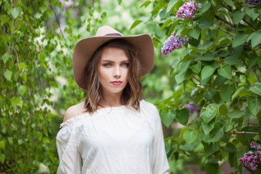 Sağlıklı, genç, esmer kadın model, taze cilt, saç kesimi ve doğal makyajla yeşil bulanık yapraklara karşı beyaz bahar çiçekli.