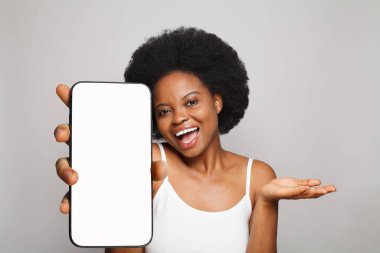 Stüdyonun arka planında beyaz boş ekran ekranı olan akıllı telefonu tutan heyecanlı bir kadın. Telefonlu mutlu model