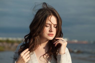 Kahverengi saçlı ve doğal makyajlı zarif genç bir bayan model bir bahar sabahı tatil köyünün kıyılarında yürüyor. Mutluluk, denge, sakinlik, duygu ve ruh hali konsepti. Gözler kapalı