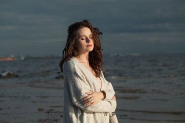 Kahverengi saçlı, doğal makyajlı ve bir bahar sabahı tatil köyünün kıyılarında yürüyen muhteşem genç kadın modeli. Mutluluk, denge, sakinlik, duygu ve ruh hali konsepti. Gözler kapalı