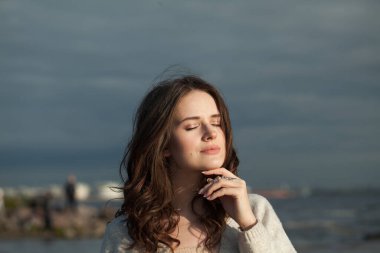 Dinlenmiş esmer kadın taze cilt, doğal makyaj ve sağlıklı dalgalı kahverengi saçlar güneşli sabah ve deniz havasının tadını çıkarıyor. Kadın model açık hava moda portresi