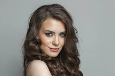 Uzun kahverengi dalgalı saçları ve makyajlı yakın plan portresi olan neşeli esmer kadın model.
