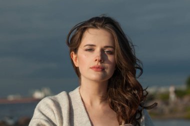 Kahverengi saçlı ve doğal makyajlı çekici genç bir bayan model bir bahar sabahı tatil köyünün kıyılarında yürüyor. Mutluluk, denge, sükunet, duygu ve ruh hali konsepti