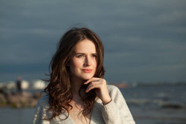 Kahverengi saçlı ve doğal makyajlı mutlu bir genç kadın model bir bahar sabahı tatil köyünün kıyılarında yürüyor. Mutluluk, denge, sükunet, duygu ve ruh hali konsepti