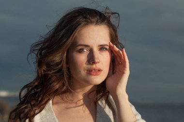 Kahverengi saçlı, doğal makyajlı, mükemmel bir genç bayan model bahar sabahı tatil köyünün kıyılarında yürüyor. Mutluluk, denge, sükunet, duygu ve ruh hali konsepti