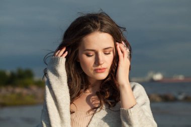 Kahverengi saçlı ve doğal makyajlı güzel bir bayan model bir bahar sabahı tatil köyünün kıyılarında yürüyor. Mutluluk, denge, sükunet, duygu ve ruh hali konsepti