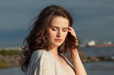 Kahverengi saçlı, doğal makyajlı ve bir bahar sabahı tatil köyünün kıyılarında yürüyen gevşemiş genç bir kadın model. Mutluluk, denge, sakinlik, duygu ve ruh hali konsepti. Gözler kapalı