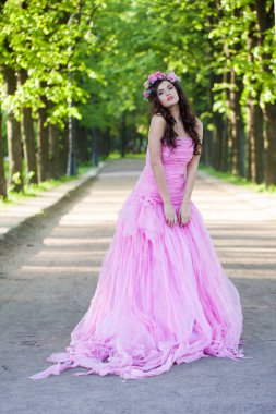 Parlak makyajlı, kıvırcık saçlı ve yeşil yapraklı pembe çiçekli güzel bir kadın model. Pembe elbiseli sağlıklı bir kadın.