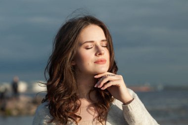 Kaygısız genç bayan esmer model deniz sahilinde. Makyajlı ve açık havada uzun siyah dalgalı saç stili olan bir kadın. Sükunet duygusu, seyahat, sezon ve tatil konsepti
