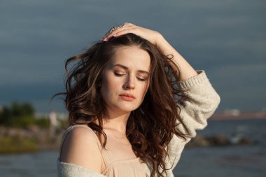 Kahverengi saçlı, doğal makyajlı ve bir bahar sabahı tatil köyünün kıyılarında yürüyen muhteşem bir genç kadın mankeni. Mutluluk, denge, sakinlik, duygu ve ruh hali konsepti. Gözler kapalı