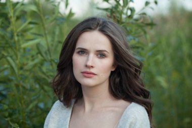 Sağlıklı esmer bir kadının yakın plan portresi. Taze, açık tenli, açık havada koyu kahverengi saçlı yeşil çimen arka planda, hava portresi.