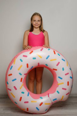 Pembe kauçuk yüzükten yüzme havuzu olan güzel bir kız çocuğu beyaz stüdyo arka planında duruyor.