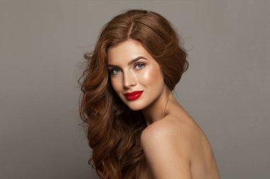 Uzun dalgalı saçları ve makyajı olan çekici, modaya uygun bir kızıl kadın. Model hanımın kırmızı renkli rujlu portresi. Saç bakımı, cilt bakımı ve renklendirme kavramı