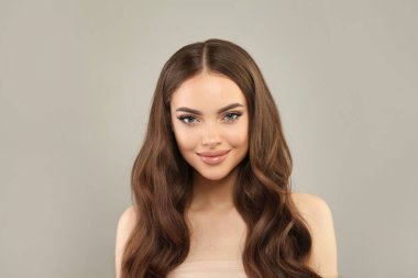 Sağlıklı saçlı, makyajlı ve parlak ciltli güzel bir bayan model gri stüdyo arka planında poz veriyor. Yüz bakımı, kozmetoloji, saç bakımı ve güzellik kadın konsepti