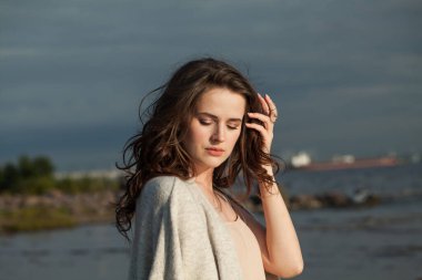 Kahverengi saçlı, doğal makyajlı ve bir bahar sabahı tatil köyünün kıyılarında yürüyen büyüleyici genç kadın modeli. Mutluluk, denge, sakinlik, duygu ve ruh hali konsepti. Gözler kapalı