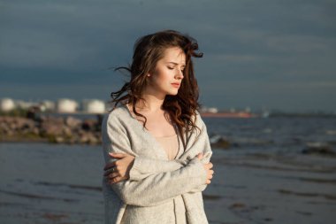 Deniz sahilinde düşünceli, esmer bir bayan model. Makyajlı ve açık havada uzun siyah dalgalı saç stili olan güzel kadın.