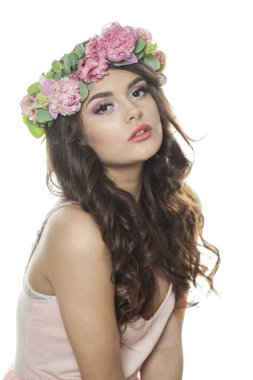 Uzun siyah dalgalı saçlı, parlak tenli, pembe çiçekli taç takan genç yaz kadını, stüdyo portresi. Kozmetik, mutluluk, güzellik ve moda kavramı