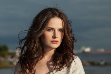 Deniz sahilinde güzel bir esmer kadın modeli. Makyajlı ve açık havada uzun siyah dalgalı saç stili olan bir kadın. Sükunet duygusu, seyahat, sezon ve tatil konsepti