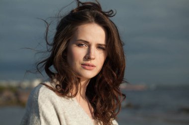 Deniz sahilinde zarif, esmer bir bayan model. Makyajlı ve açık havada uzun siyah dalgalı saç stili olan bir kadın. Sükunet duygusu, seyahat, sezon ve tatil konsepti