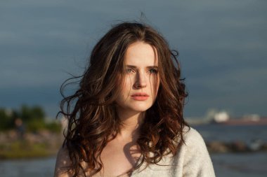 Deniz sahilinde güzel, esmer bir bayan model. Makyajlı ve açık havada uzun siyah dalgalı saç stili olan bir kadın. Sükunet duygusu, seyahat, sezon ve tatil konsepti