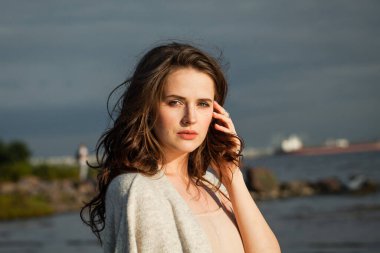 Deniz sahilinde genç ve güzel bir esmer model. Makyajlı ve açık havada uzun siyah dalgalı saç stili olan bir kadın. Sükunet duygusu, seyahat, sezon ve tatil konsepti