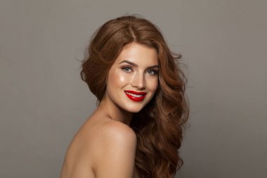 Sağlıklı saçlı, makyajlı ve parlak ciltli neşeli bir bayan model gri stüdyo arka planında poz veriyor. Yüz bakımı, kozmetoloji, saç bakımı ve güzellik kadın konsepti