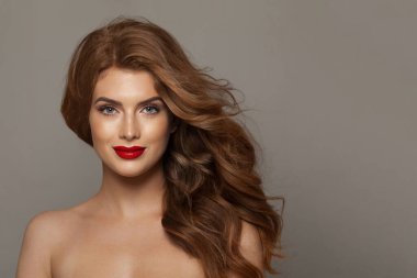 Sağlıklı saçlı, makyajlı ve parlak ciltli göz alıcı genç bir bayan model gri stüdyo arka planında poz veriyor. Yüz bakımı, kozmetoloji, saç bakımı ve güzellik kadın konsepti