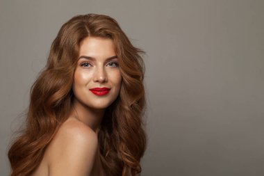 Güzel, genç ve mutlu bir kadın modeli, doğal makyajlı, temiz ve sağlıklı bir cildi ve gri arka planda uzun saçları var. Kıvırcık, saç bakımı, cilt bakımı ve yüz bakımı konsepti