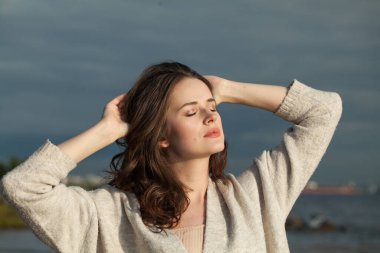 Taze tenli, doğal makyajlı, sağlıklı dalgalı kahverengi saçlı, güneşli sabahın ve deniz havasının tadını çıkaran esmer bir kadın. Kadın model açık hava moda portresi