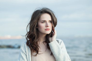 Düşünceli esmer kadın taze cilt, doğal makyaj ve sağlıklı dalgalı kahverengi saçlar güneşli sabah ve deniz havasının tadını çıkarıyor. Kadın model açık hava moda portresi