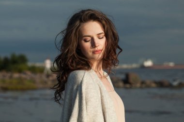 Kahverengi saçlı ve doğal makyajlı romantik bir genç bayan model bir bahar sabahı tatil köyünün kıyılarında yürüyor. Mutluluk, denge, sakinlik, duygu ve ruh hali konsepti. Gözler kapalı