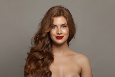 Uzun dalgalı saçları ve makyajı olan hoş, şık, kızıl bir kadın. Model hanımın kırmızı renkli rujlu portresi. Saç bakımı, cilt bakımı ve renklendirme kavramı