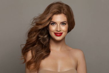 Doğal makyajlı, sağlıklı ciltli ve gri arka planda poz veren güzel, genç ve mutlu bir kadın modeli. Kıvırcık, saç bakımı, cilt bakımı ve yüz bakımı konsepti