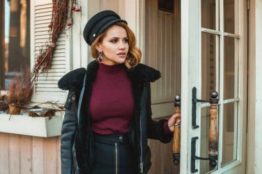 Güzel, düşünceli, siyah deri ceketli kadın şehir sokaklarında dikiliyor.