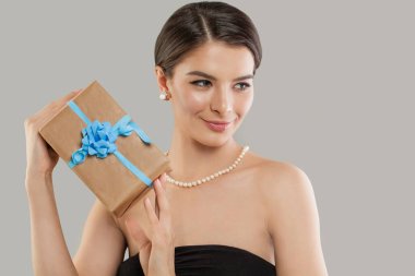 Gri arka planda bej renkli hediye kutusunu tutan mutlu bir kadın. Güzellik stüdyosu portresini kapat.