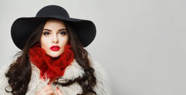 Beyaz stüdyo duvarına poz veren parlak makyajlı, uzun dalgalı saçlı, eski moda genç kadın model.
