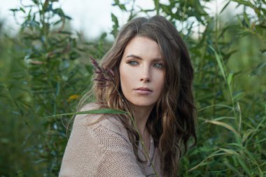 Temiz tenli, doğal makyajlı, yeşil çimen arka planında kıvırcık saçlı, çekici, genç model bir kadın.