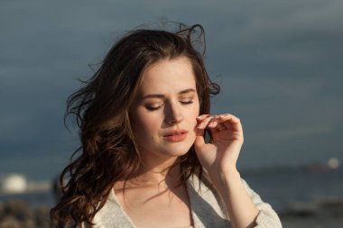 Deniz sahilinde genç bayan esmer model. Makyajlı ve açık havada uzun siyah dalgalı saç stili olan bir kadın. Sükunet duygusu, seyahat, sezon ve tatil konsepti