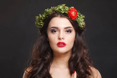 Çiçekli başlıklı muhteşem genç kadın siyah arka planda dikilirken kameraya bakıyor.