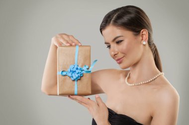 Güzel bir model kadın hediye kutusunu elinde tutuyor ve gri arka planda şu ana bakıyor.
