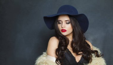 Uzun siyah dalgalı saç stili ve kırmızı dudaklı çekici manken kadın şık bir şapka stüdyo resmi giyiyor.