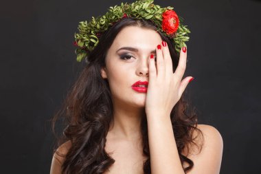 Çiçekli kafa çelengi olan hoş bir kadın siyah arka planda dikilirken kameraya bakıyor.