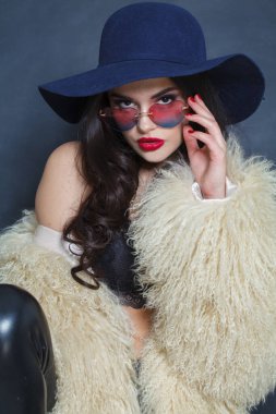 Makyajlı, uzun kıvırcık saçlı, mavi arka planda poz veren genç, esmer kadın. Moda güzellik stüdyosu portresi. Güzel kadın yüzü. Yakından.