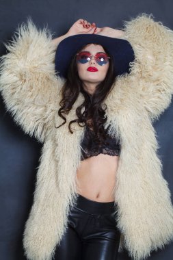 Makyajlı, uzun kıvırcık saçlı, mavi arka planda poz veren genç esmer kadın, moda güzellik stüdyosu portresi.