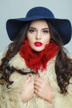 Makyajlı, uzun kıvırcık saçlı, mavi arka planda poz veren şık, genç esmer bayan, moda güzellik stüdyosu portresi. Güzel kadın yüzü. Yakından.