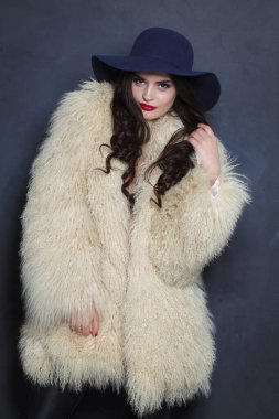 Makyajlı, uzun kıvırcık saçlı, mavi arka planda poz veren güzel esmer bayan, moda stüdyosu resmi.