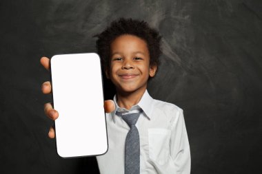 Elinde cep telefonu olan gülümseyen küçük okul çocuğu mavi stüdyo arka planında akıllı telefon boş ekran görüntüsü sunuyor. Akıllı telefon görüntüleme modeli