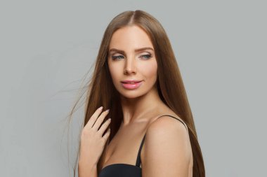 Modern makyajlı ve uzun düz saç stili beyaz stüdyo arka planında duran neşeli genç kadın modeli.