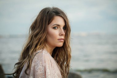 Rüzgarlı kahverengi saçlı, açık havada yürüyen düşünceli, genç bir kadın model.